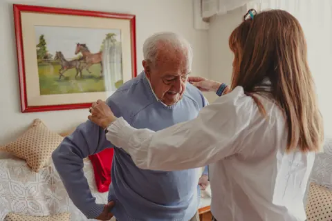 Pflegekraft hilft einem Senior beim Anziehen des Pullovers